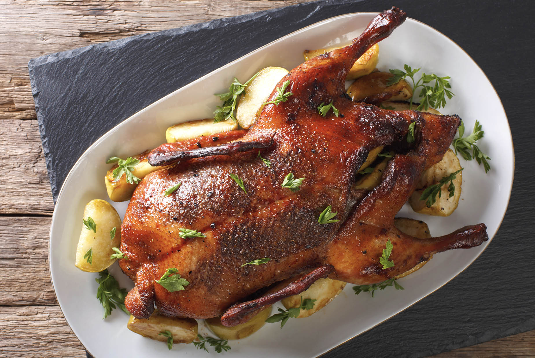 Delicious whole baked duck with apples close-up on a platter on the table. horizontal view from above 